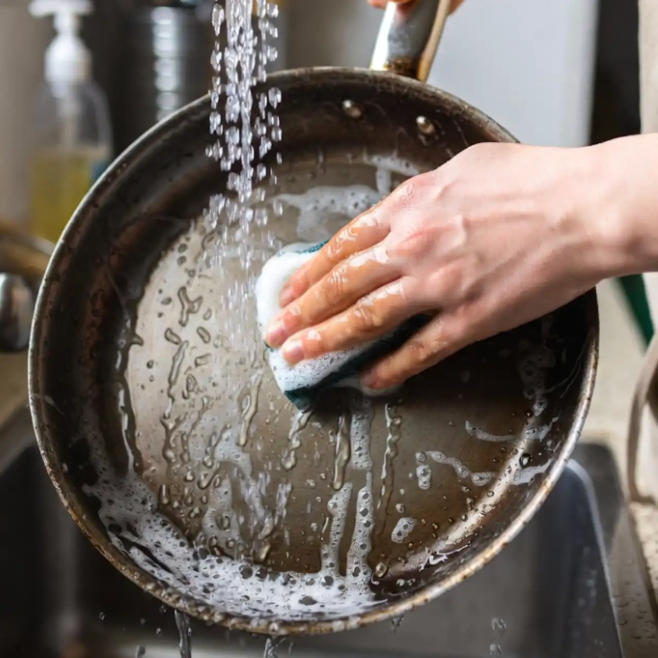 Hombre lavando una sartén de hierro fundido nueva con agua caliente y jabón, usando una esponja.
