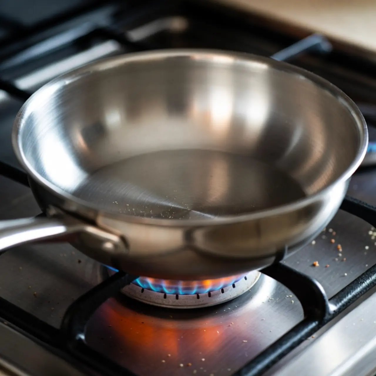 Sartén de acero inoxidable vacía sobre un quemador de gas a fuego medio-alto.