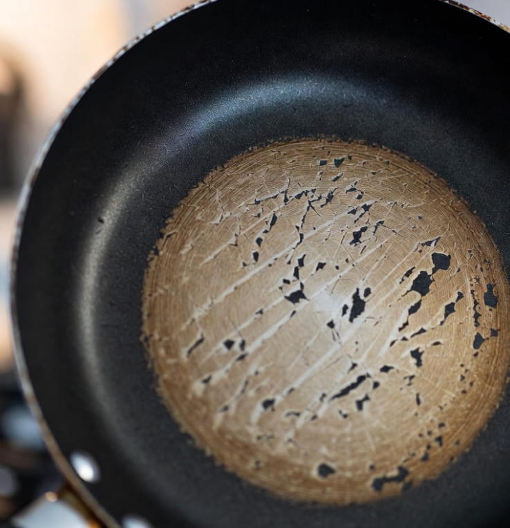 Primer plano de una sartén antiadherente con la capa de teflón claramente rayada y desconchada